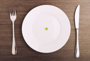 diet concept. one pea on an empty white plate with knife and fork
